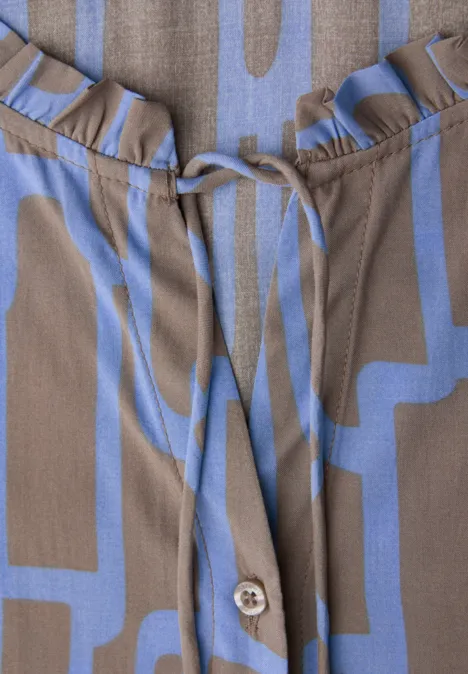 Nahaufnahme einer taupefarbenen Bluse mit abstraktem blau-lila Muster, Rüschen am Ausschnitt und Tunnelzug.